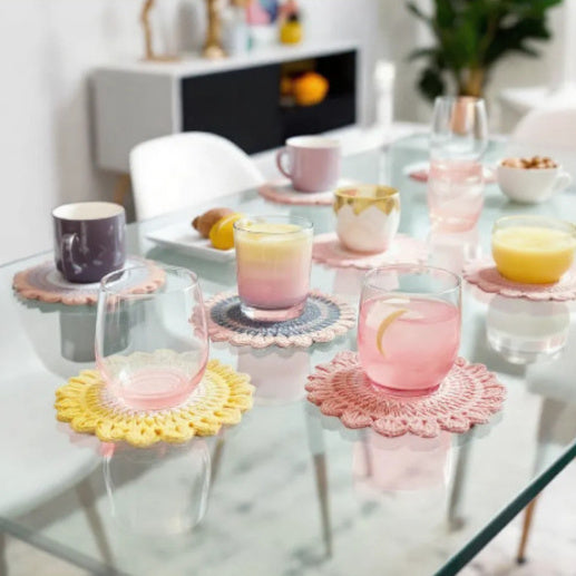 sottobicchieri ad uncinetto colorati su una tavola di vetro con bicchieri sopra