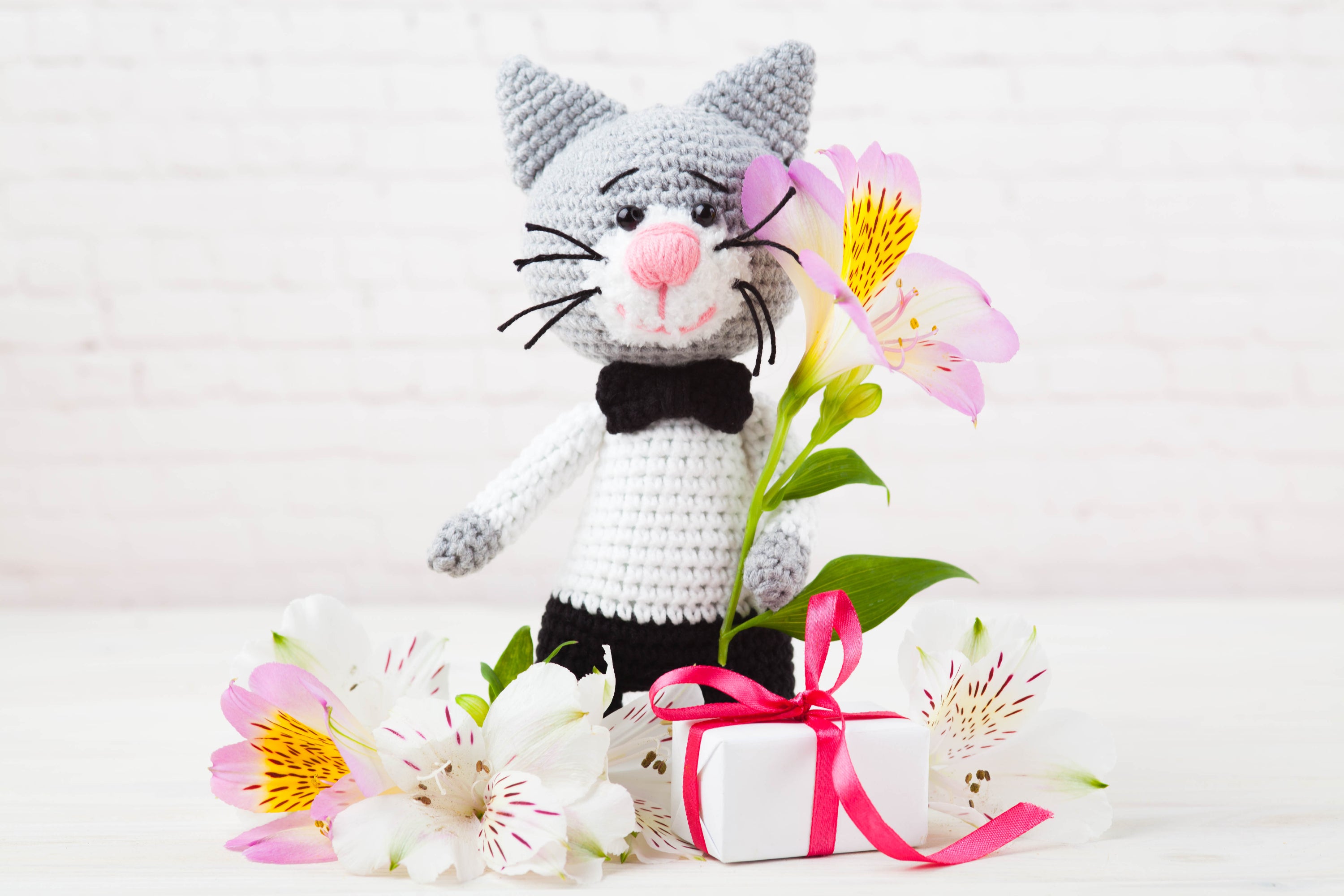 gatto ad uncinetto realizzato con la tecnica dell'amigurumi con fiori e regalo